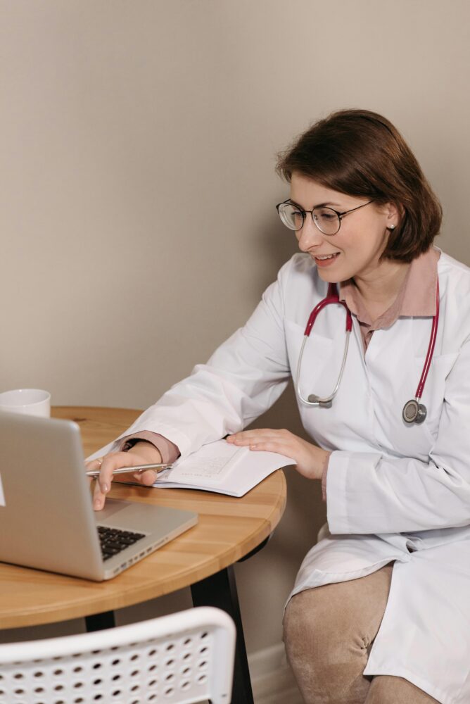 Doctor using a computer, smiling and talking to a pacient via telehealth.